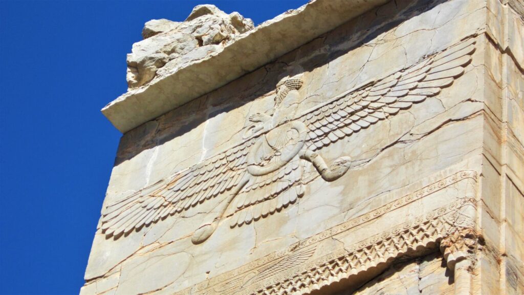 Skrzydła i pierścień faravahara wykute w kamiennej belce budowli w Persepolis, widziane od dołu na tle nieba